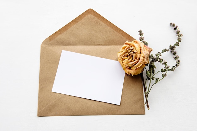 Una busta fatta di carta kraft una carta bianca bianca e fiori secchi su un tavolo bianco Vista dall'alto di sfondo vacanza alla moda