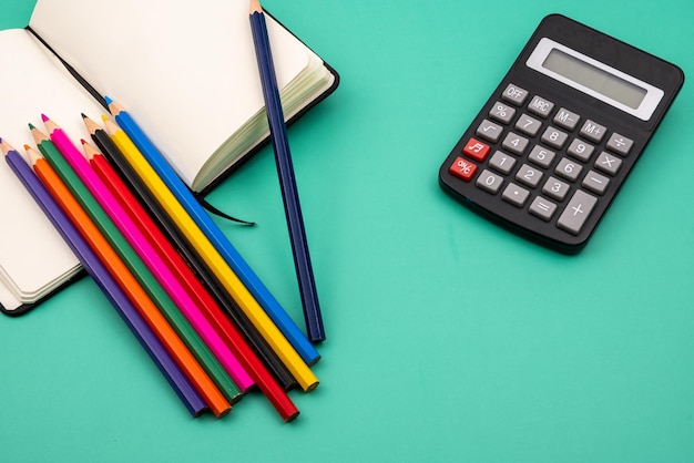 Una calcolatrice con diversi pennarelli e matite colorate su un tavolo verde.