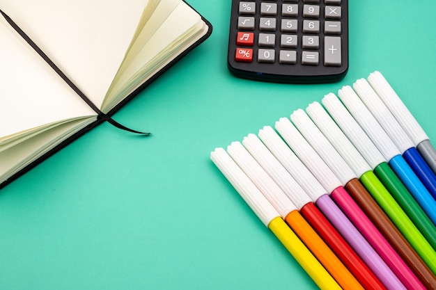 Una calcolatrice con diversi pennarelli e matite colorate su un tavolo verde.