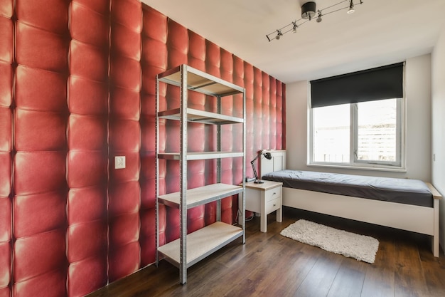 una camera da letto con carta da parati rossa sulle pareti e scaffali bianchi di fronte al letto c'è una piccola finestra