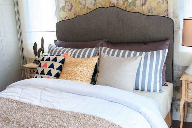 Una camera da letto dal design interno con cuscini colorati sul letto e moderna lampada sul cassetto.