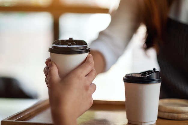 Una cameriera che tiene e serve bicchieri di carta di caffè caldo al cliente al bar