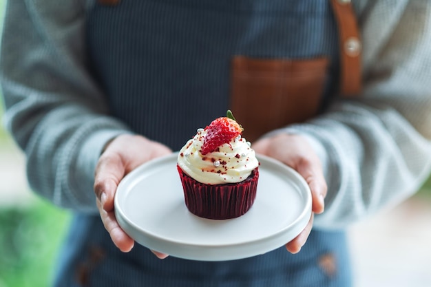 Una cameriera che tiene e serve un pezzo di cupcake di velluto rosso