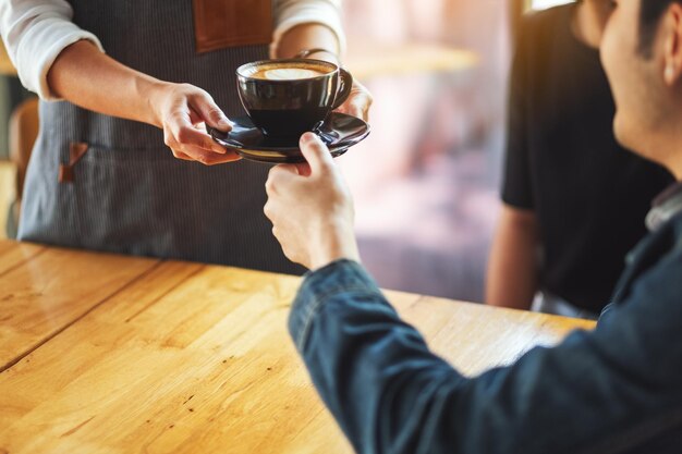 Una cameriera che tiene e serve una tazza di caffè caldo a un cliente maschio al bar