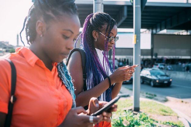 Una camminata di due sorelle delle donne all'aperto facendo uso dello smartphone