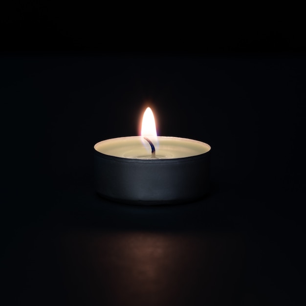 Una candela accesa su una parete scura con un bagliore in primo piano.