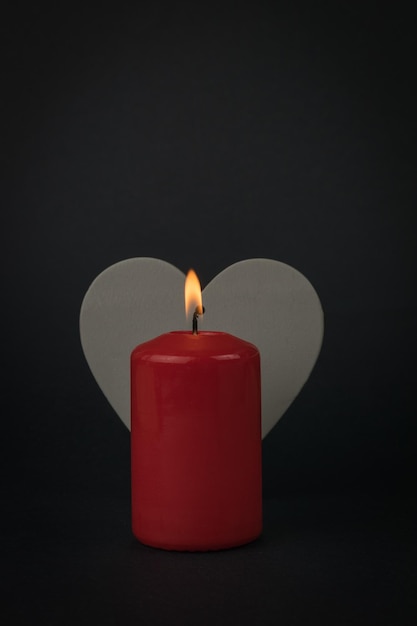 Una candela con uno stoppino acceso sullo sfondo di un cuore di legno grigio. Il concetto di una relazione romantica.
