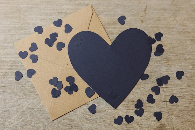 una carta bianca a forma di cuore nero con confetti di carta nera su un'enveloppa marrone su un tavolo di legno