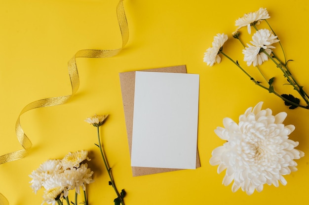 Una carta bianca con una busta e dei fiori è posta su uno sfondo giallo