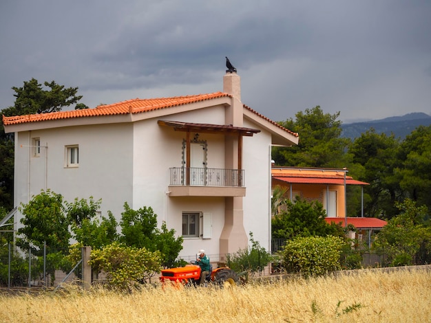 Una casa in un villaggio greco contro e un uomo su un trattore arancione in un campo in Grecia