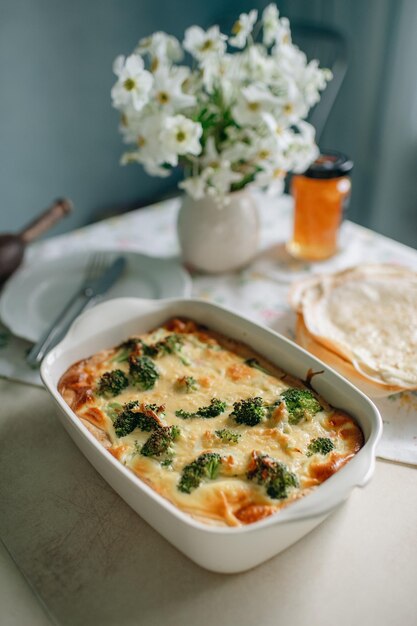 Una casseruola di broccoli e formaggio con un fiore bianco sullo sfondo.