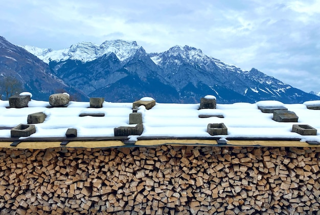 Una catasta di legna è coperta di neve e le montagne sono coperte di neve.