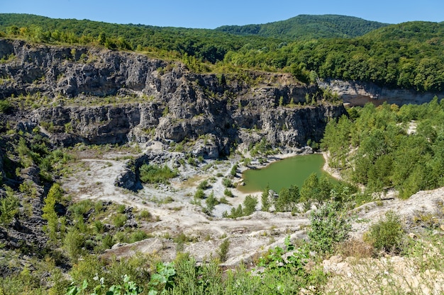 Una cava di granito abbandonata ricoperta di alberi con un lago verde in fondo. Natura e paesaggi dell'Adighezia