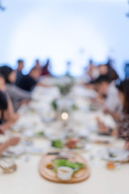 Una cena sfocata con il proiettore e lo schermo bianco per il pubblico asiatico siedono nella lunga fila del tavolo