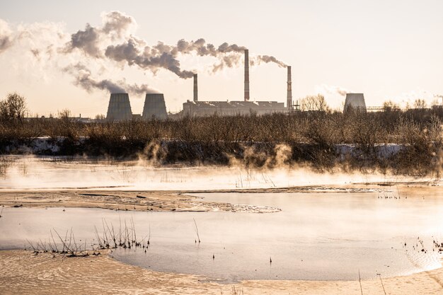 Una centrale elettrica rilascia sostanze inquinanti nell'aria e in uno specchio d'acqua. Inquinamento ambientale