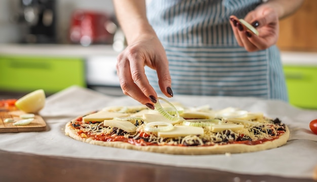 Una chef donna con un grembiule sta mettendo anelli di cipolla su una pizza cruda