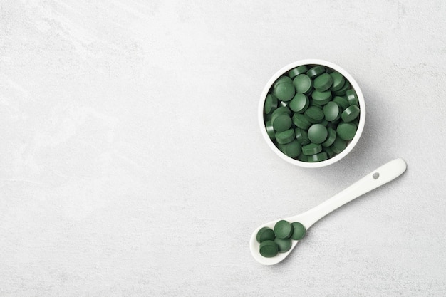 Una ciotola con compresse di spirulina su sfondo grigio, un posto per il testo