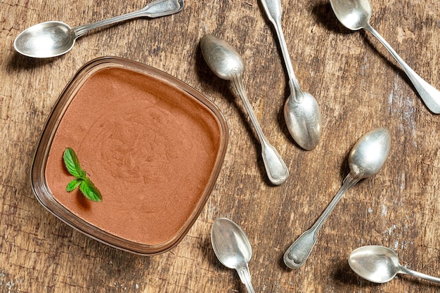 Una ciotola con la tradizionale mousse al cioccolato francese con una foglia di menta e molti cucchiai vista dall'alto