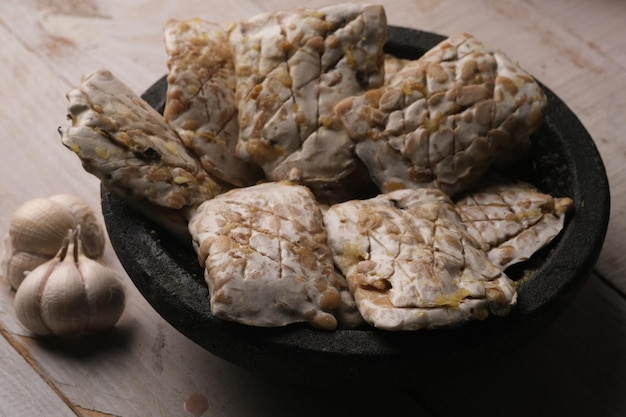 Una ciotola di cibo con accanto un cucchiaio tempeh crudo marinato con sale di coriandolo all'aglio su mortaio