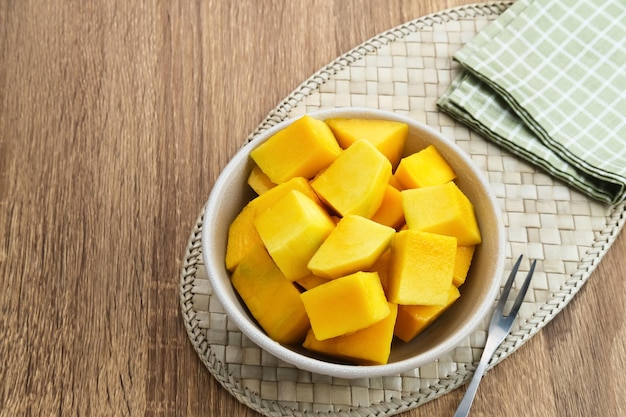 Una ciotola di cubetti di mango fresco affettato su fondo di legno.