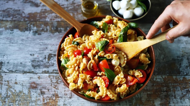 Una ciotola di insalata di pasta con un cucchiaio di legno.