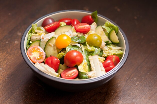 una ciotola di insalata verde con un salso di vinaigrette sano, cetriolo e pomodori.