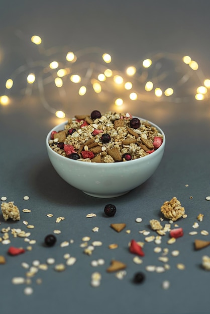 Una ciotola di muesli su uno sfondo grigio monocromatico, con piume bianche e un lato da una ghirlanda. Ehi