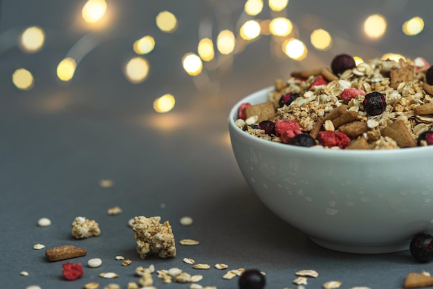 Una ciotola di muesli su uno sfondo grigio monocromatico, con piume bianche e un lato da una ghirlanda. Ehi