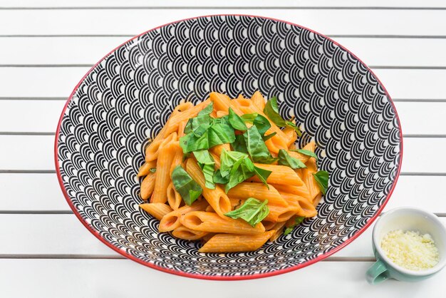 Una ciotola di penne con foglie di basilico su un tavolo di legno bianco.