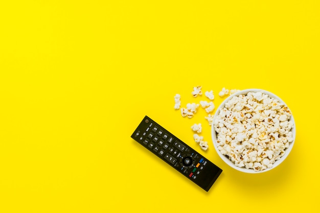 Una ciotola di popcorn e telecomando TV su uno sfondo giallo. Il concetto di guardare la TV, film, serie TV, sport, spettacoli. Vista piana, vista dall'alto.