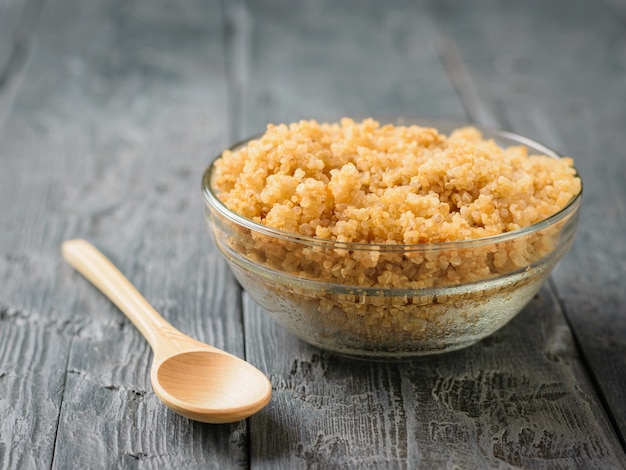 Una ciotola di quinoa bollita e un cucchiaio di legno su un tavolo di legno nero