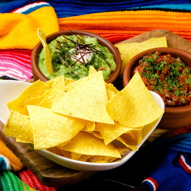 Una ciotola di tortilla chips e una ciotola di guacamole siedono su una coperta colorata.