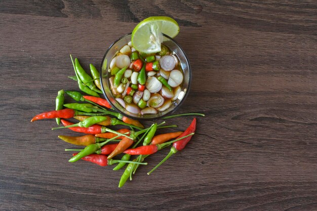 Una ciotola di verdure su un tavolo con peperoncino rosso e spicchi di lime.