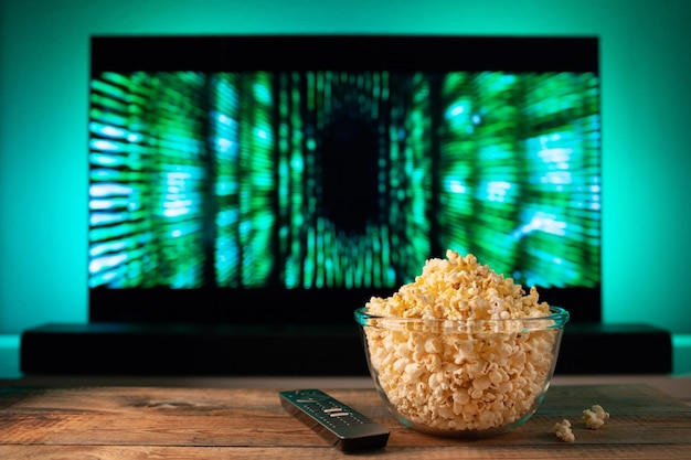 Una ciotola di vetro di popcorn e telecomando in sottofondo la tv funziona