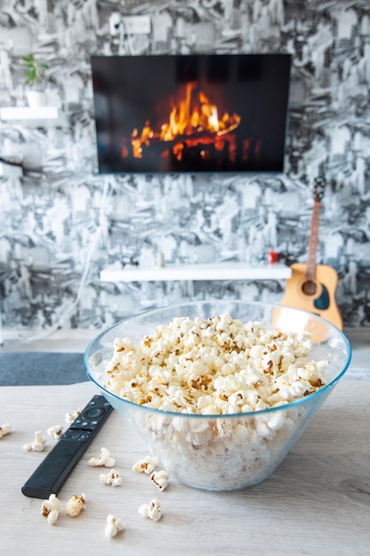 Una ciotola di vetro di popcorn e un telecomando sullo sfondo la TV funziona Serata accogliente guardando un film o una serie TV a casa