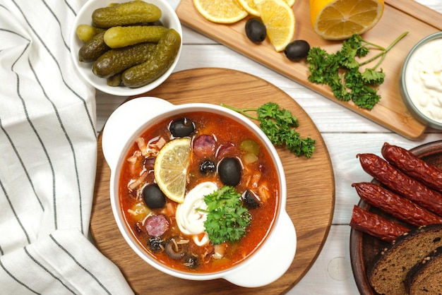 Una ciotola di zuppa di pesce con una ciotola di olive e una ciotola di sottaceti su un tavolo di legno.