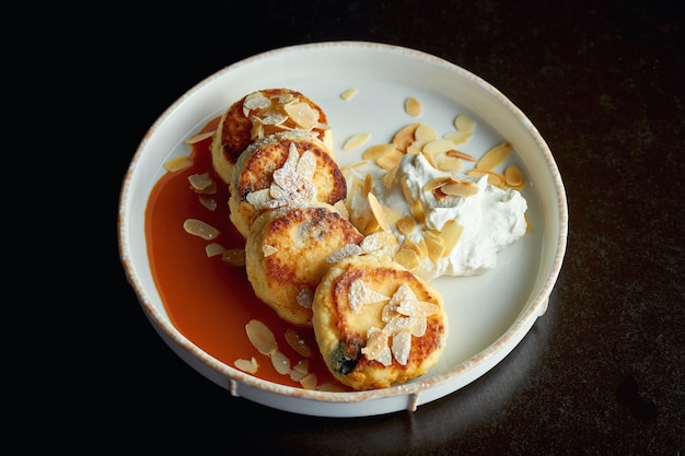 Una colazione ideale - Frittelle di ricotta con caramello, mandorle e salsa di panna in un piatto bianco. Syrniki ucraino