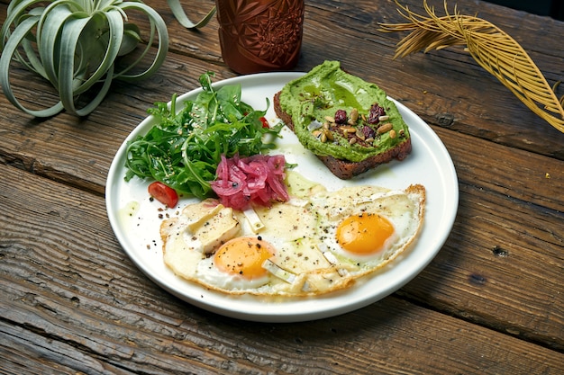 Una colazione sana ed equilibrata - uova strapazzate con camembert, insalata di rucola e toast di avocado. Tavolo in legno