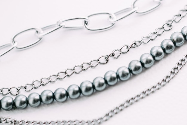 Una collana di perline grigie con decori a catena su fondo estetico bianco