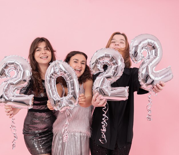 Una compagnia di amiche allegre su uno sfondo rosa da studio con palloncini d'argento sotto forma di numeri 2022.