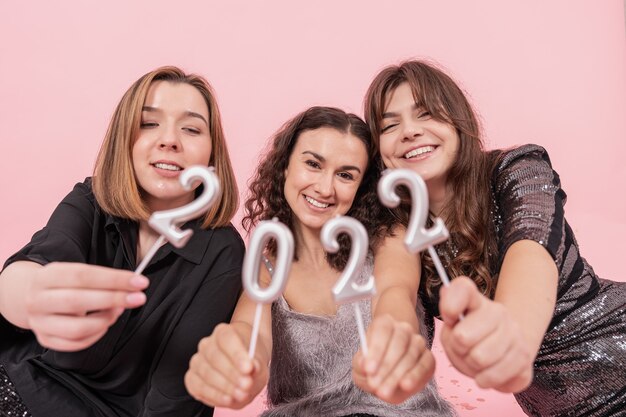 Una compagnia di amiche allegre su uno sfondo rosa tiene i numeri 2022, festa di Capodanno, festa di Natale.