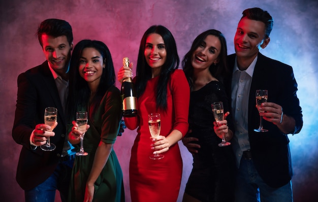 Una compagnia di cinque persone giovani e attraenti sta facendo una festa, godendosi la compagnia l'una dell'altra, bevendo champagne e posando insieme ai flauti