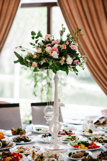 Una composizione di fiori e verde è su un tavolo festivo presso la sala del banchetto di nozze Stand numero di segno Primo piano
