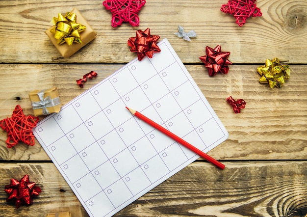Una composizione di Natale con un aliante o un calendario la mano di una donna che tiene una matita Archi e regali su uno sfondo di legno Il concetto di Natale e Capodanno