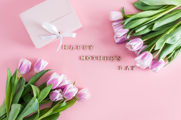 Una composizione festiva con tulipani viola e testo in lettere di legno di Happy Mother's Day vista dall'alto stile piatto sfondo rosa