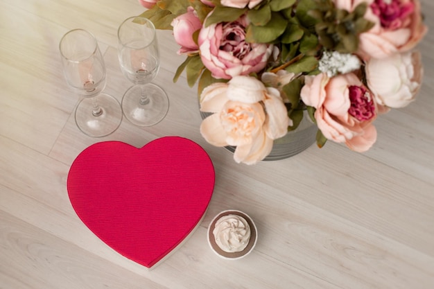 Una confezione regalo a forma di cuore rosso e un mazzo di fiori sono sul pavimento di San Valentino