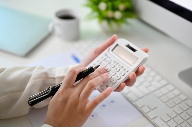Una contabile femminile che utilizza la calcolatrice per calcolare le vendite e il profitto che lavora alla sua scrivania