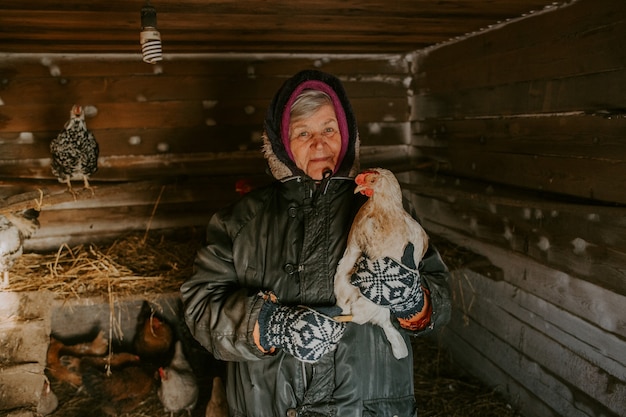 Una contadina anziana tiene in mano un pollo