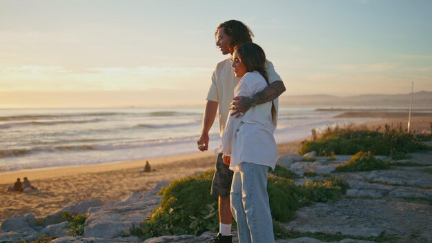 Una coppia adolescente si gode il tramonto, l'oceano, giovani amanti che si abbracciano, vacanze d'estate romantiche.