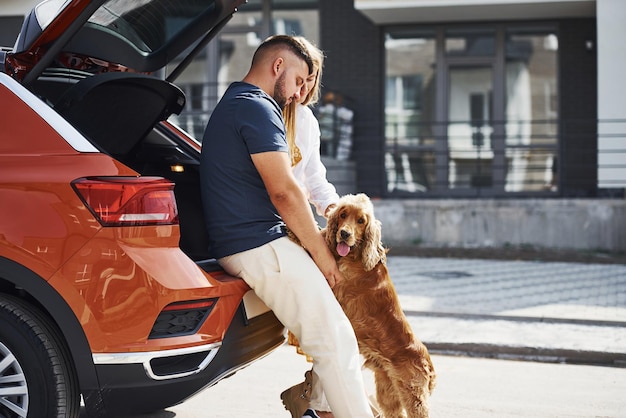 Una coppia adorabile fa una passeggiata insieme al cane all'aperto vicino all'auto.